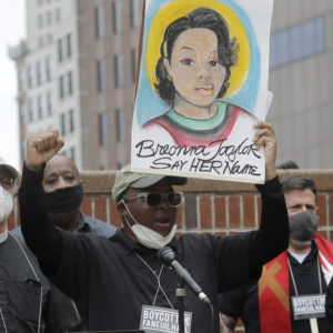 Kevin Peterson, founder and executive director of The New Democracy Coalition, center, displays a placard showing fallen Breonna Taylor as he addresses a rally, Tuesday, June 9, 2020, in Boston. Petersen advocates for changing the name of Faneuil Hall, as its namesake Peter Faneuil, was a slave owner. (AP Photo/Steven Senne)